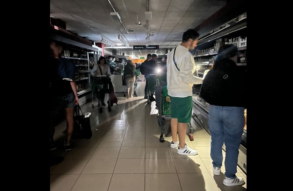 Mai multe persoane stau la coadă pe întuneric, într-un magazin, în timpul penei masive de curent care a cuprins Spania, Portugalia și Franța