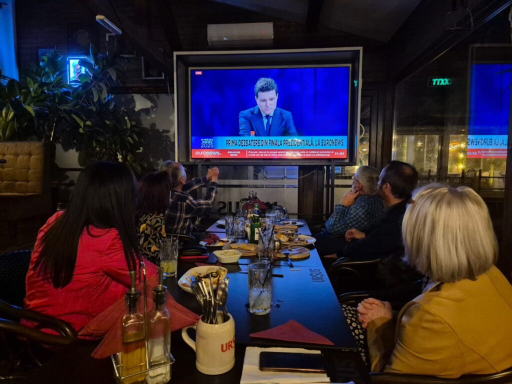 Mai multe persoane urmăresc dezbaterea electorală dintre Nicușor Dan și George Simion, într-un local din Buzău