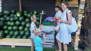 O mamă cu doi copii este în fața unei tarabe cu pepeni, din Suceava