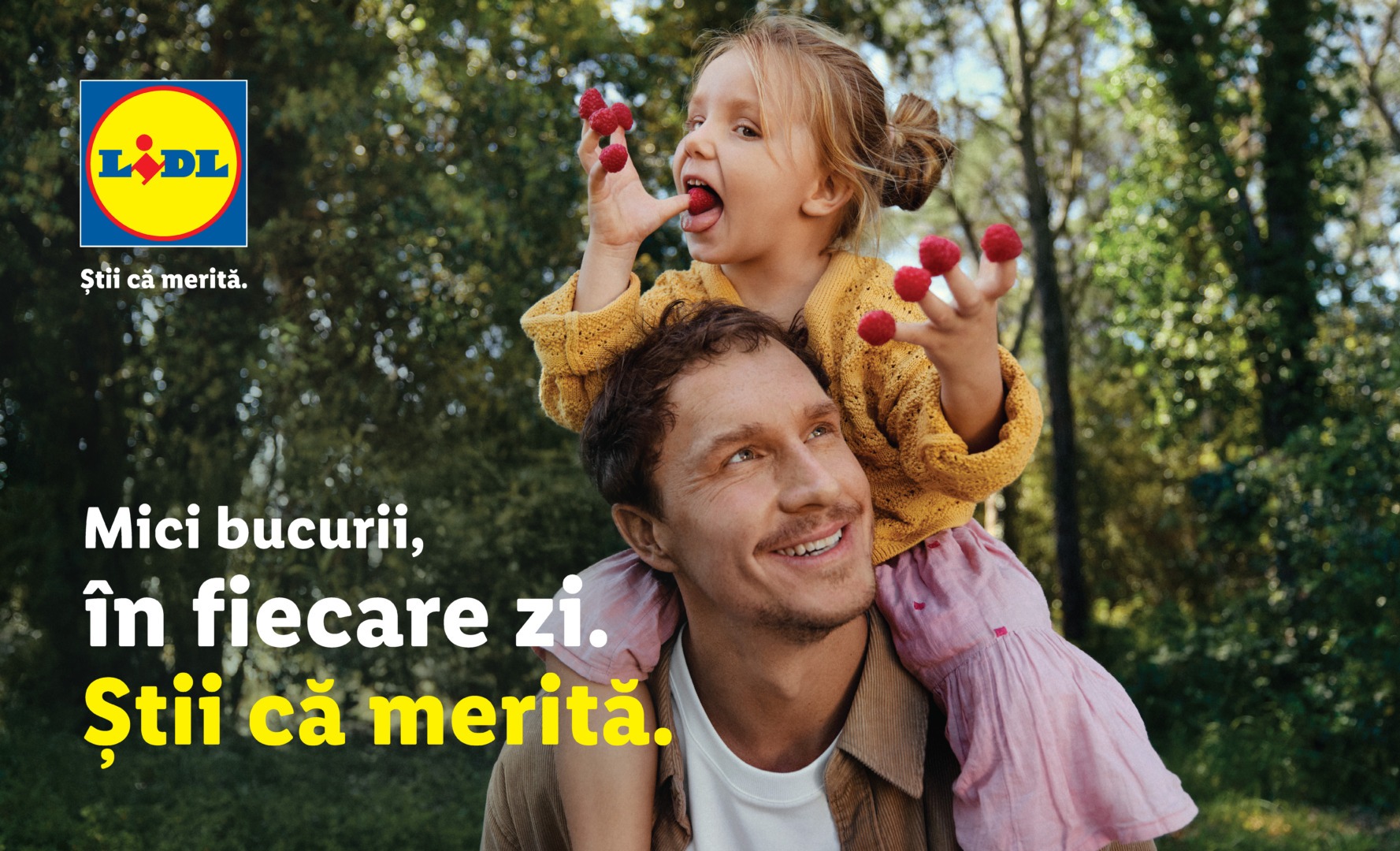 Un barbat cu o fetita tinuta pe umeri, care mananca frute